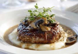 Homemade Salisbury steak served with rich mushroom gravy, mashed potatoes, and fresh parsley garnish on a dinner plate.