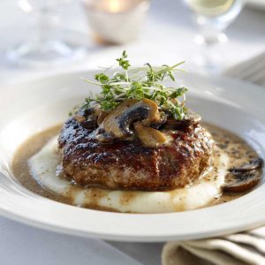 Homemade Salisbury steak served with rich mushroom gravy, mashed potatoes, and fresh parsley garnish on a dinner plate.