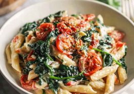Creamy spinach tomato pasta with penne, fresh spinach, cherry tomatoes, and a rich garlic cream sauce served in a rustic bowl.