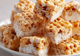 Chewy marshmallow cereal treats made with honeycomb cereal, cut into squares and stacked on a plate with a gooey texture.