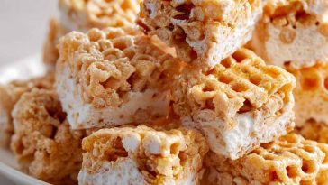 Chewy marshmallow cereal treats made with honeycomb cereal, cut into squares and stacked on a plate with a gooey texture.
