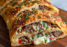 Mozzarella Cheese Steak Stromboli with golden-brown crust, filled with sliced steak, melted mozzarella, sautéed onions and peppers, served sliced on a plate.