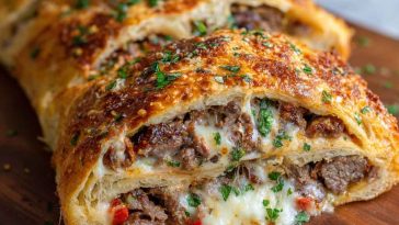Mozzarella Cheese Steak Stromboli with golden-brown crust, filled with sliced steak, melted mozzarella, sautéed onions and peppers, served sliced on a plate.