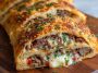 Mozzarella Cheese Steak Stromboli with golden-brown crust, filled with sliced steak, melted mozzarella, sautéed onions and peppers, served sliced on a plate.