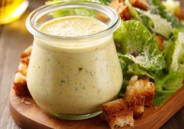 Homemade Caesar dressing in a glass jar with parmesan cheese, garlic, and lemon on a wooden table