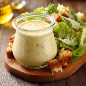 Homemade Caesar dressing in a glass jar with parmesan cheese, garlic, and lemon on a wooden table