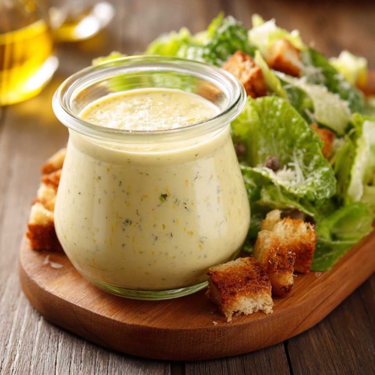 Homemade Caesar dressing in a glass jar with parmesan cheese, garlic, and lemon on a wooden table