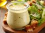 Homemade Caesar dressing in a glass jar with parmesan cheese, garlic, and lemon on a wooden table