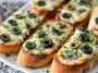 Toasted French bread topped with melted cheese, sliced olives, and herbs, served as a savory appetizer.