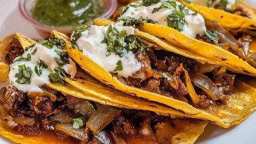 Authentic quesabirria tacos filled with tender beef birria, melted cheese, and fresh cilantro, served with a side of consommé for dipping.