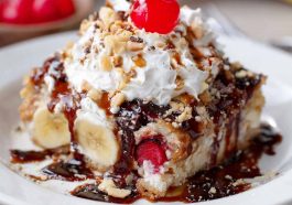 Banana split dump cake topped with melted chocolate, cherries, and whipped cream served in a baking dish.