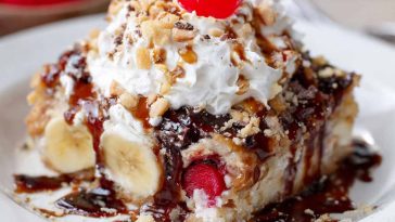 Banana split dump cake topped with melted chocolate, cherries, and whipped cream served in a baking dish.
