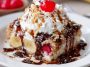 Banana split dump cake topped with melted chocolate, cherries, and whipped cream served in a baking dish.