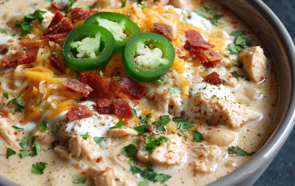 Creamy white cheddar apple chicken chili served in a bowl with melted cheese, apple slices, and fresh herbs