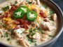 Creamy white cheddar apple chicken chili served in a bowl with melted cheese, apple slices, and fresh herbs