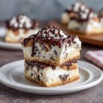 Creamy cannoli cheesecake bars topped with mini chocolate chips and powdered sugar on a golden graham cracker crust.