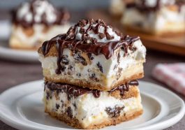 Creamy cannoli cheesecake bars topped with mini chocolate chips and powdered sugar on a golden graham cracker crust.