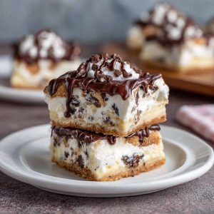Creamy cannoli cheesecake bars topped with mini chocolate chips and powdered sugar on a golden graham cracker crust.