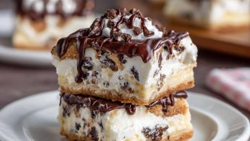 Creamy cannoli cheesecake bars topped with mini chocolate chips and powdered sugar on a golden graham cracker crust.