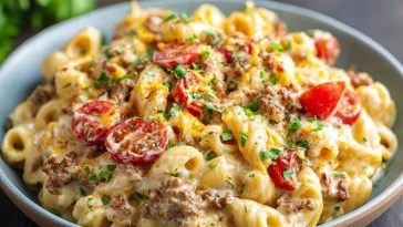 A hearty skillet of creamy loaded cheeseburger Alfredo pasta topped with melted cheese, ground beef, crispy bacon, and fresh parsley.
