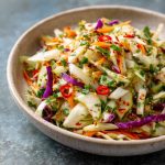 A colorful bowl of sweet and spicy pickle slaw made with shredded cabbage, carrots, and chopped pickles, garnished with fresh herbs.