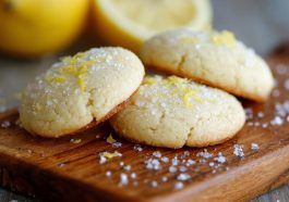 A plate of golden lemon sugar cookies sprinkled with sugar crystals, garnished with lemon zest and served on a rustic white dish.