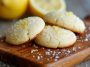 A plate of golden lemon sugar cookies sprinkled with sugar crystals, garnished with lemon zest and served on a rustic white dish.