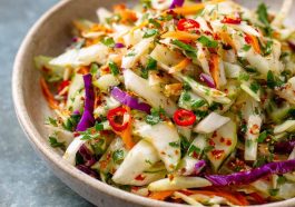 A colorful bowl of sweet and spicy pickle slaw made with shredded cabbage, carrots, and chopped pickles, garnished with fresh herbs.