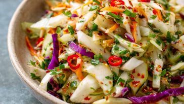 A colorful bowl of sweet and spicy pickle slaw made with shredded cabbage, carrots, and chopped pickles, garnished with fresh herbs.