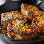 Garlic butter pan-seared pork chops with a golden crust, topped with herbs and a rich buttery sauce.
