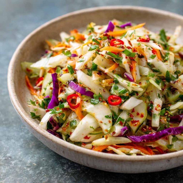 A colorful bowl of sweet and spicy pickle slaw made with shredded cabbage, carrots, and chopped pickles, garnished with fresh herbs.
