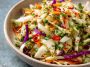 A colorful bowl of sweet and spicy pickle slaw made with shredded cabbage, carrots, and chopped pickles, garnished with fresh herbs.