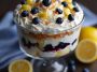 A layered lemon blueberry trifle in a glass bowl, with fluffy cake cubes, lemon cream, fresh blueberries, and whipped topping, garnished with lemon zest.