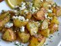 Golden roasted potatoes topped with crumbled feta, fresh herbs, and lemon slices, served in a rustic baking dish.