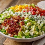 A colorful chopped salad topped with crispy bacon, fresh vegetables, shredded cheese, and drizzled with creamy ranch dressing.