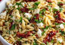A colorful bowl of orzo pasta salad with crumbled feta, sun-dried tomatoes, fresh herbs, and a light vinaigrette, served in a rustic dish.