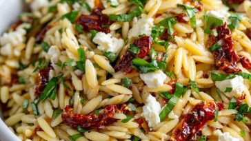 A colorful bowl of orzo pasta salad with crumbled feta, sun-dried tomatoes, fresh herbs, and a light vinaigrette, served in a rustic dish.
