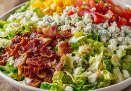 A colorful chopped salad topped with crispy bacon, fresh vegetables, shredded cheese, and drizzled with creamy ranch dressing.