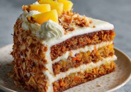 A moist Hawaiian carrot pineapple cake topped with cream cheese frosting, garnished with crushed pineapple and shredded coconut on a rustic cake stand.