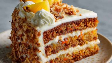 A moist Hawaiian carrot pineapple cake topped with cream cheese frosting, garnished with crushed pineapple and shredded coconut on a rustic cake stand.
