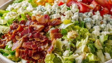 A colorful chopped salad topped with crispy bacon, fresh vegetables, shredded cheese, and drizzled with creamy ranch dressing.