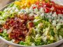 A colorful chopped salad topped with crispy bacon, fresh vegetables, shredded cheese, and drizzled with creamy ranch dressing.