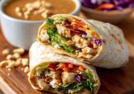Fresh Thai peanut chicken wraps filled with grilled chicken, crunchy vegetables, and drizzled with creamy peanut sauce, served on a wooden board.
