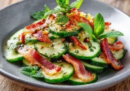 Fresh cucumber salad with crispy bacon slices, herbs, and a light creamy dressing in a bowl.