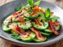 Fresh cucumber salad with crispy bacon slices, herbs, and a light creamy dressing in a bowl.