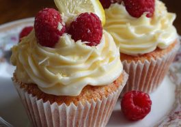 Fluffy raspberry lemon cupcakes topped with creamy frosting, fresh raspberries, and a drizzle of lemon glaze, arranged on a dessert stand.