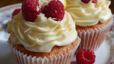 Fluffy raspberry lemon cupcakes topped with creamy frosting, fresh raspberries, and a drizzle of lemon glaze, arranged on a dessert stand.