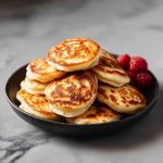 Stack of fluffy mini pancakes topped with berries and syrup