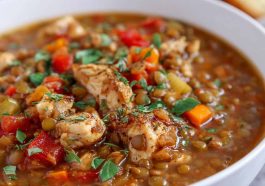 A hearty bowl of chicken lentil soup filled with tender chicken pieces, lentils, carrots, and fresh herbs, served with crusty bread on the side.