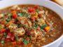 A hearty bowl of chicken lentil soup filled with tender chicken pieces, lentils, carrots, and fresh herbs, served with crusty bread on the side.